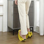 Person using yellow foot exercisers on a wooden floor with a gray cabinet in the background.